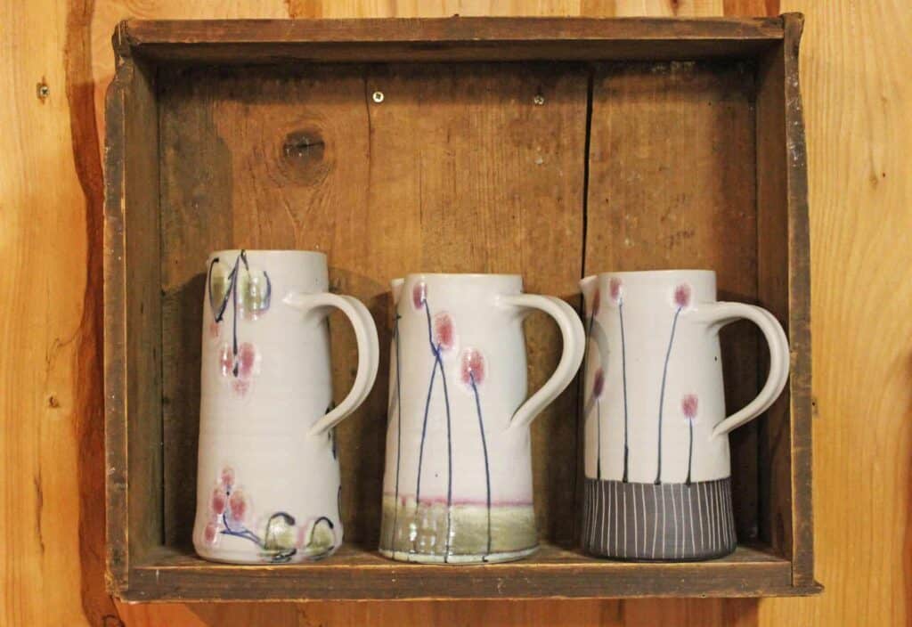 Two ceramic vases and two handmade poppies in wooden wall displays.