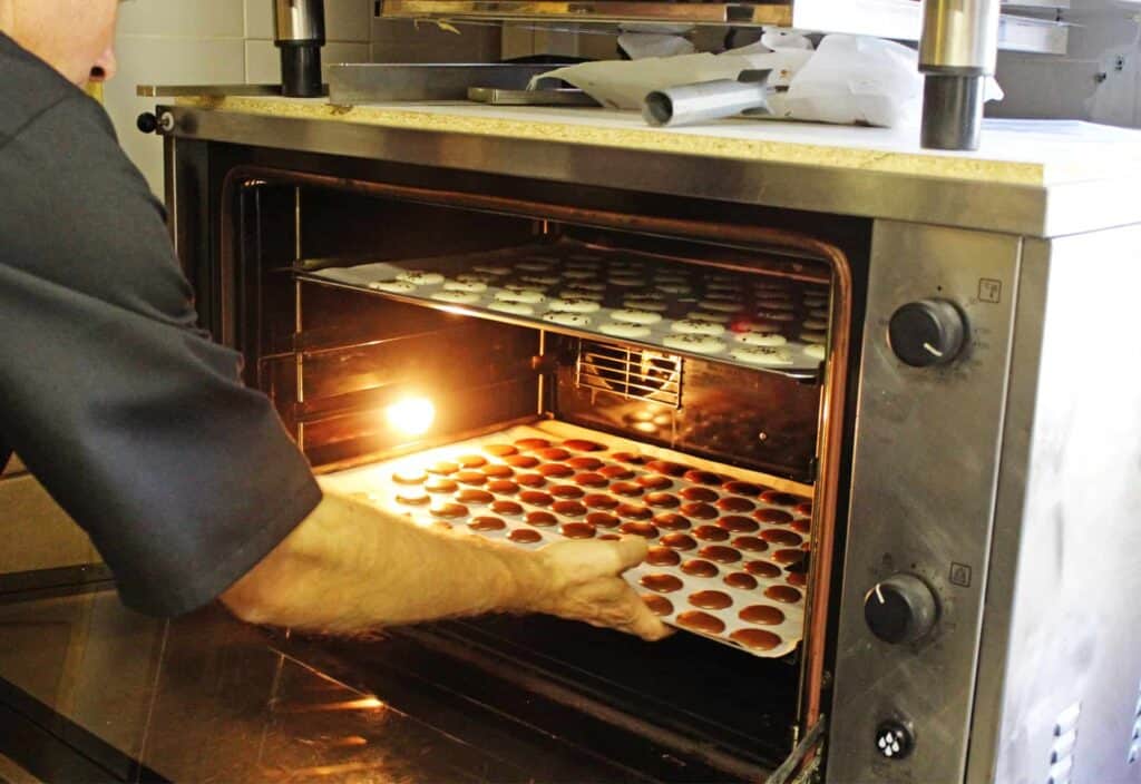 Frédéric putting two trays of macaron cases into the oven