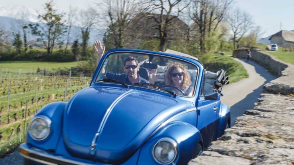 Michelle and Damien from 1786.Travel waving from a blue Volkswagen Coccinelle in the French countryside.