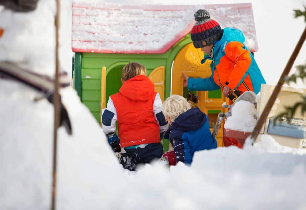 Three children playing with a wendy house in the snow