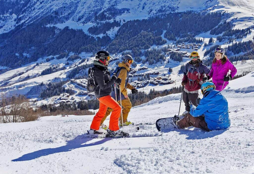 A group of skiers and snowboarders sitting and standing on the piste at Valmorel