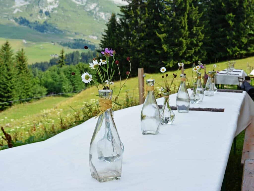 A white table with vases of wild mountain flowers in an alpine meadow