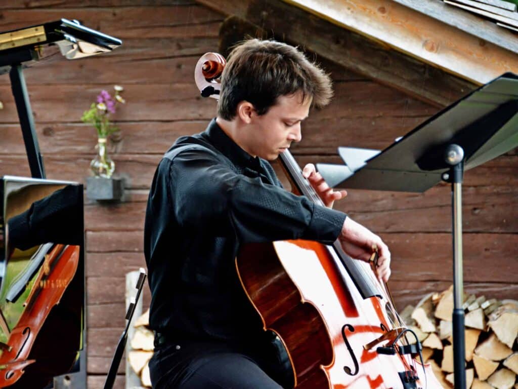 A musician playing the cello in front of an alpine chalet at the childrens music festival, Musique a beauregard