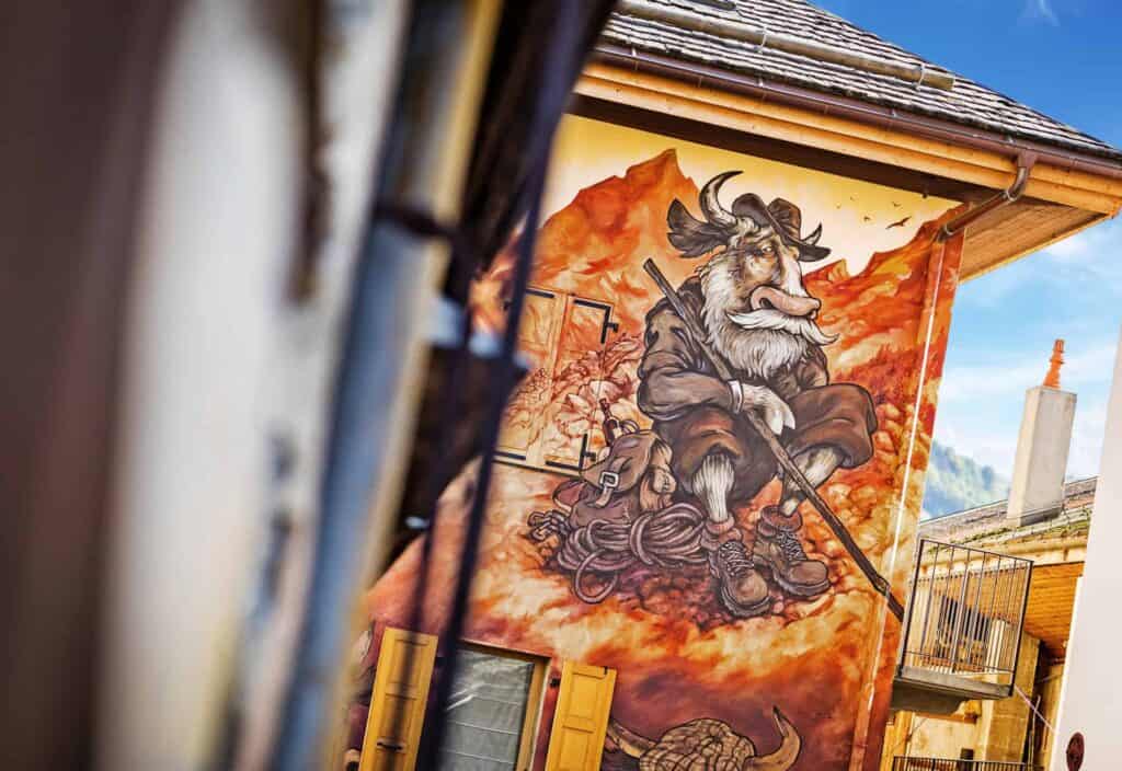 Street art on the side of a house in Le Grand Bornand depicting a cartoon cow in farmers garb