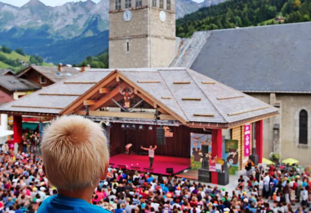 Young child watching a performance with a crowd from above around the place d'elgise in Le Grand Bornand