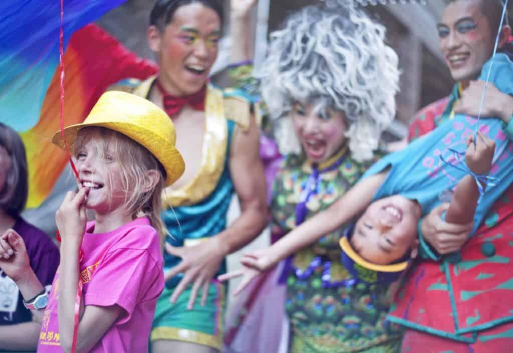 Colourfully dressed performers and children laughing at the Bonheur des Mômes festival in Le Grand Bornand