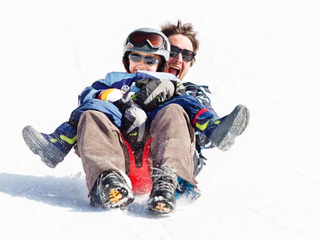 A father and son laughing while sledging in Manigod