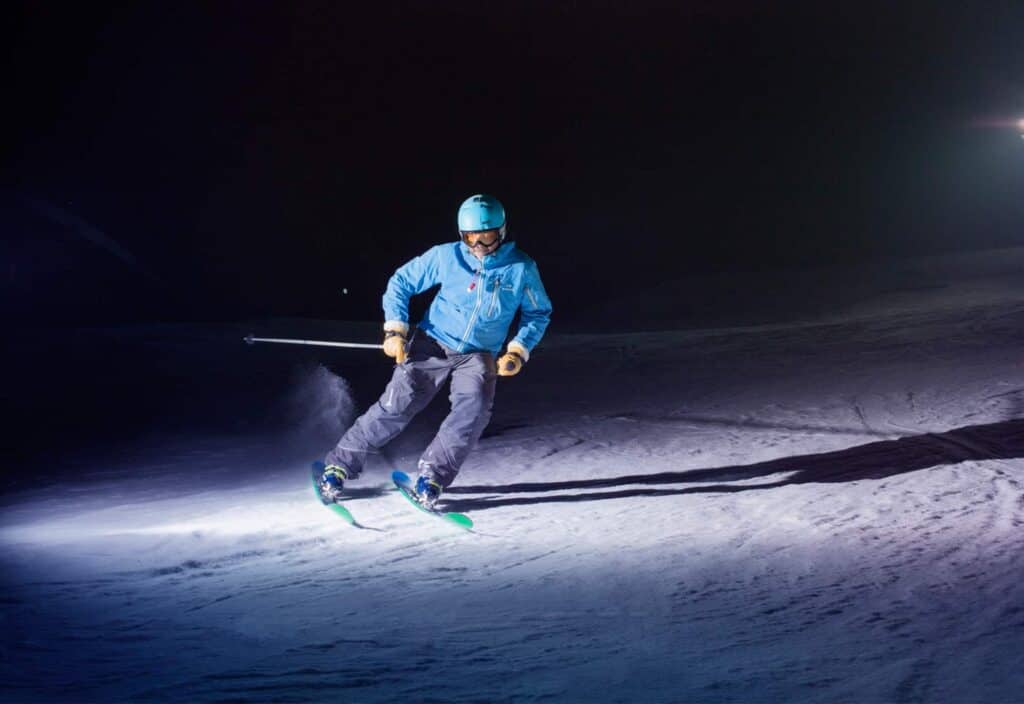 A skier carving on a floodlit piste at the Manigod night skiing