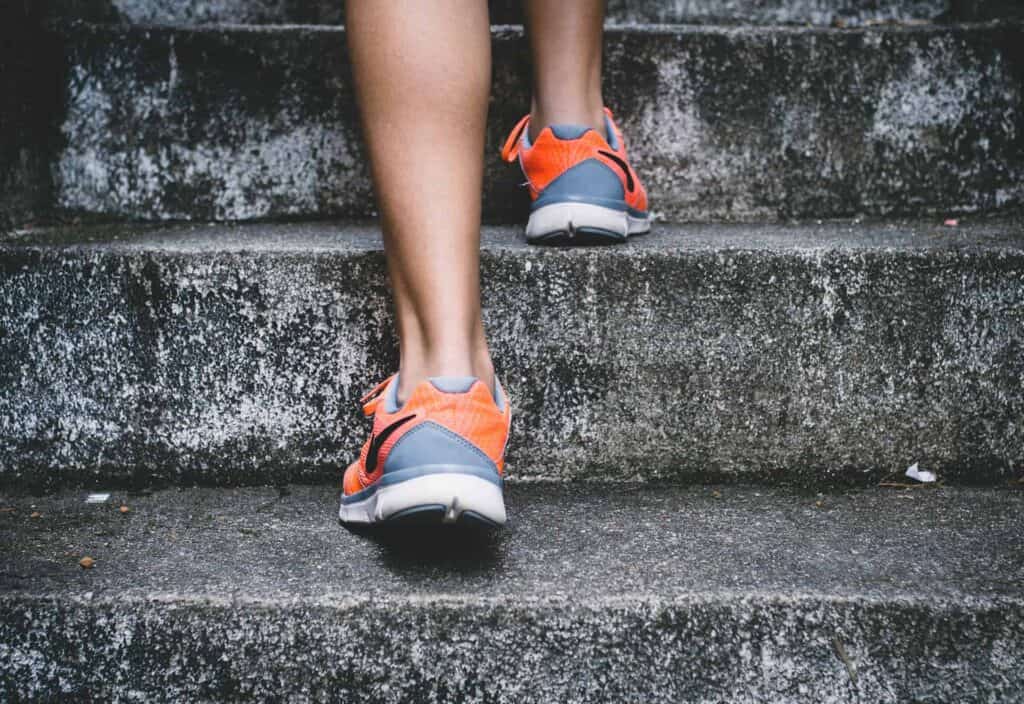 A woman's feet and ankles in grey and orange trainers doing step ups as part of her pre ski holiday exercises