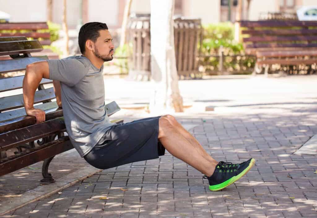 An athletic man doing tricep dips on a park bench