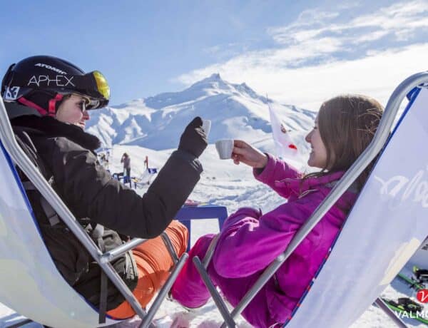 A couple toasting coffee cups while sat in ski gear on reclining chairs with snow covered mountains of Valmorel in the background