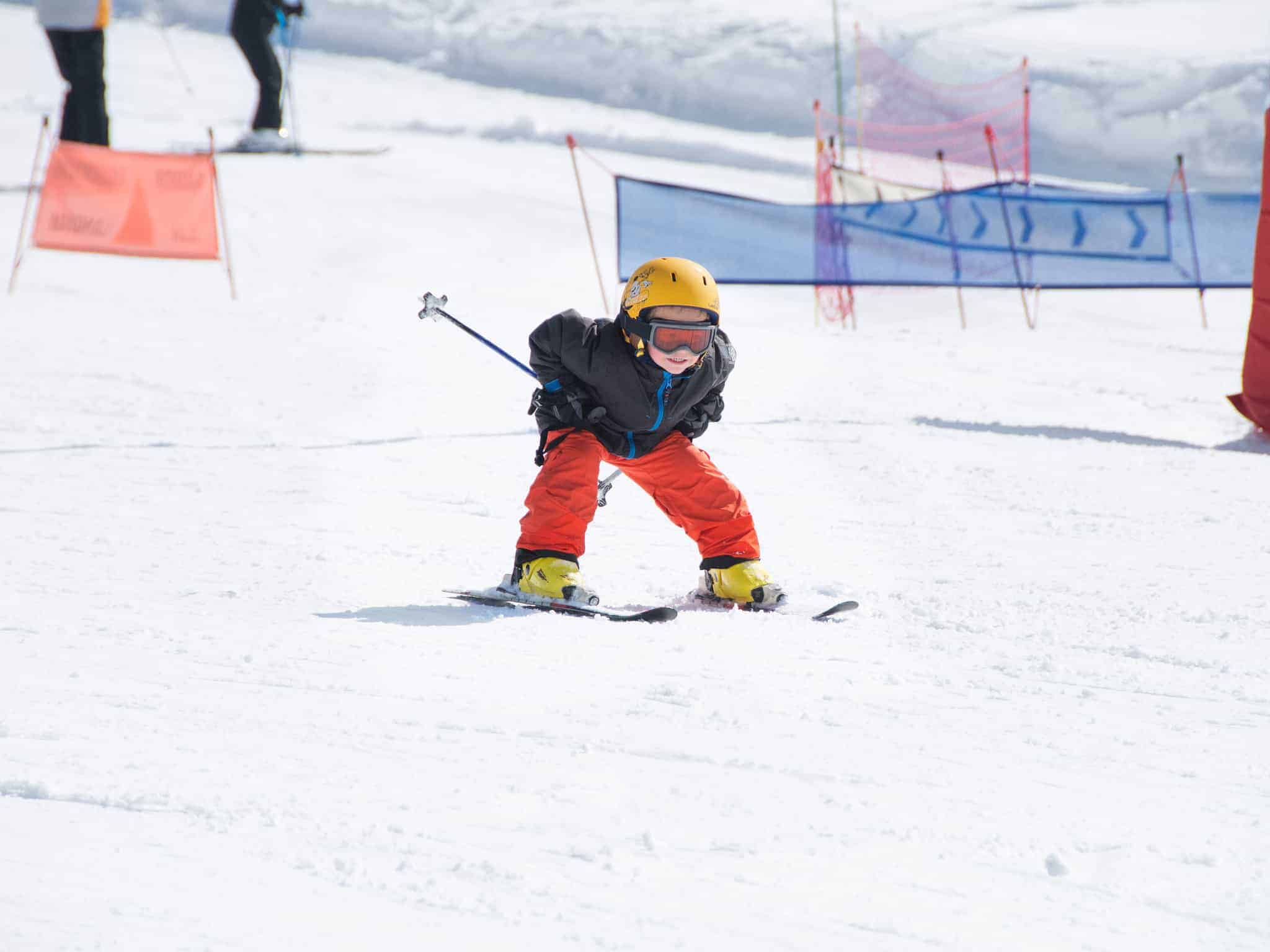 A young child wearing bright colours skiing down the ski slopes.