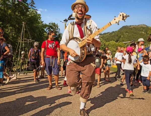 A laughing man playing a banjo with a crowd behind him on a sunny day at the family-friendly event fete de la musique