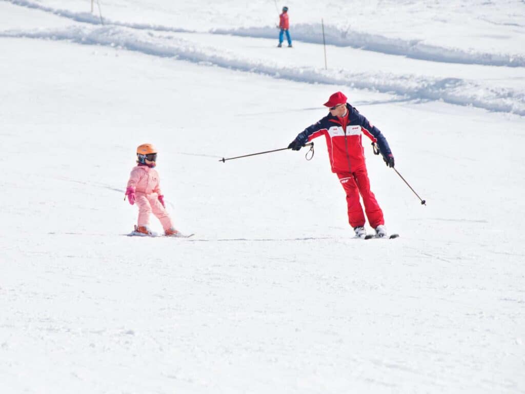 Une petite fille portant une combinaison de ski rose lors d'un cours avec l'ESF à Manigod. 