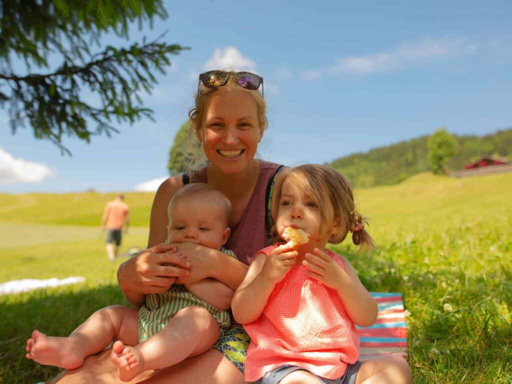 Maman avec un bébé et un enfant en bas âge assis dans un champ pendant leurs vacances d'été en famille à la montagne