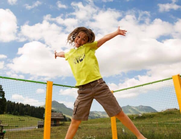 Jeune garçon en plein saut sur un trampoline pendant ses vacances d'été en famille à la montagne