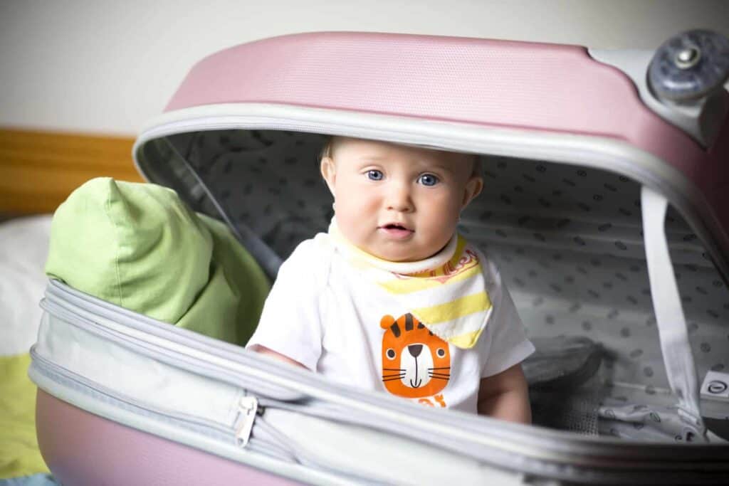 Petite fille ravie en train de faire sa valise pour ses vacances d'été en famille. Assise dans la valise parmi les vêtements.