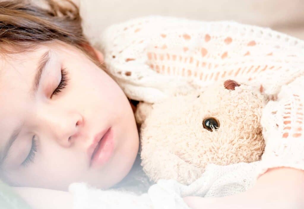 Petite fille en pyjama profondément endormie dans son lit avec une peluche dans une propriété adaptée aux familles