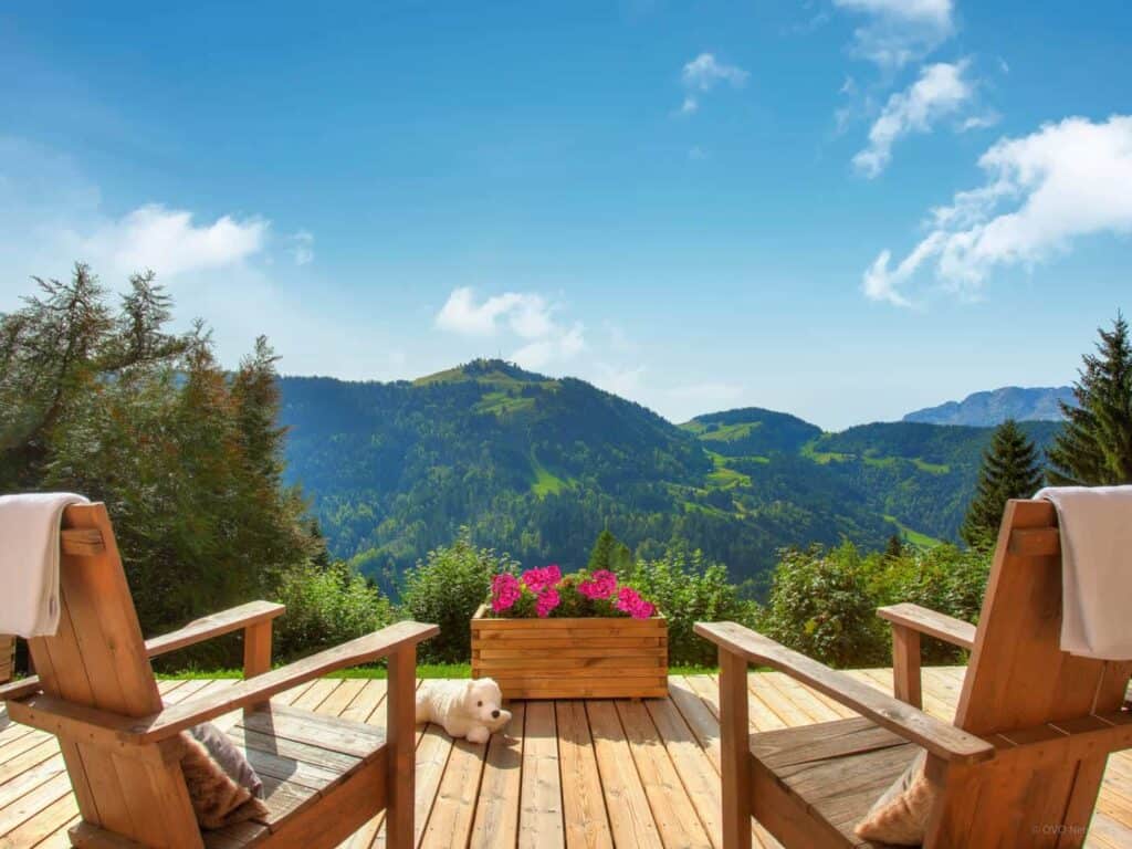 Fauteuils en bois pour profiter du panorama depuis la terrasse fleurie d'un chalet de montagne.