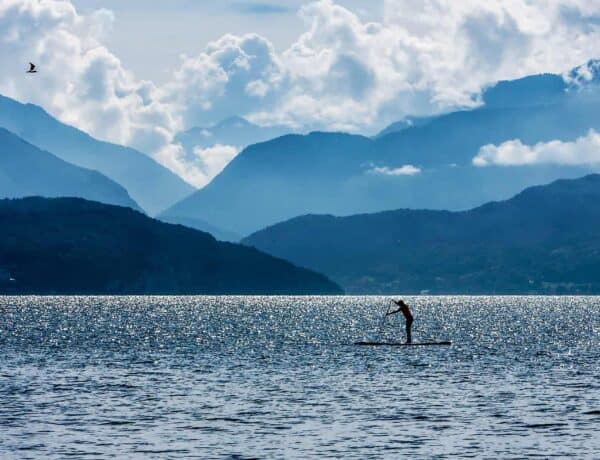 A lone stand-up paddle boarder on Lake Annecy with clouded mountains in view