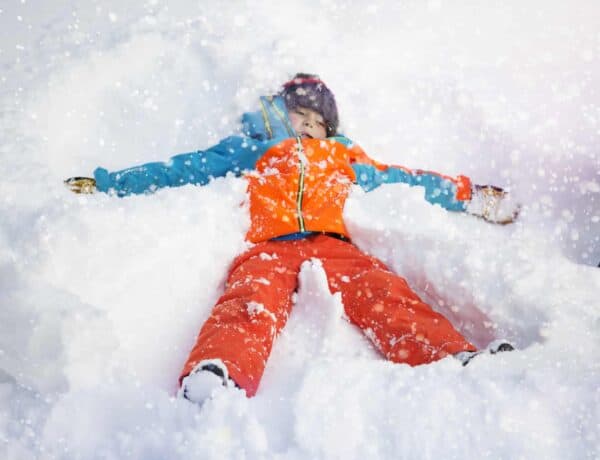 A kid wearing ski gear making a snow angel in deep snow