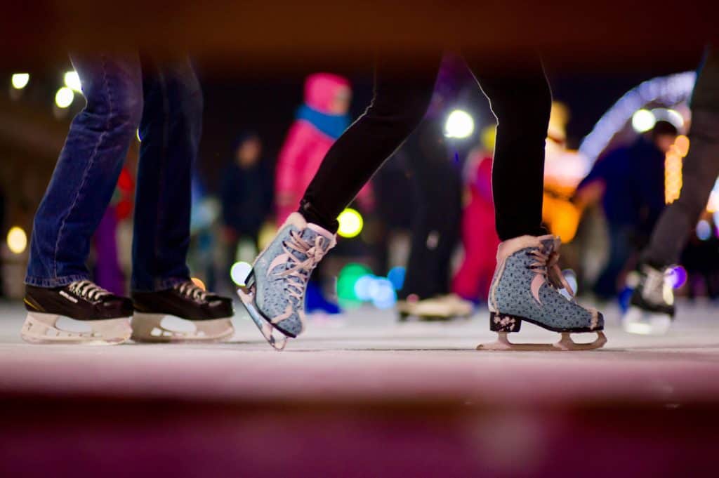 A view of ice skater's feet as they skate by a fence