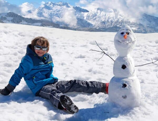 A happy young boy sitting next to his snowman in the French Alps