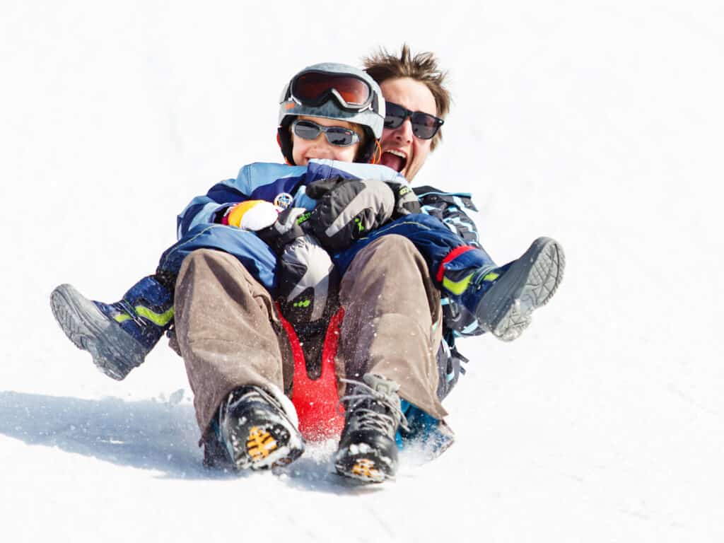 A man and a young boy sledge down a slope