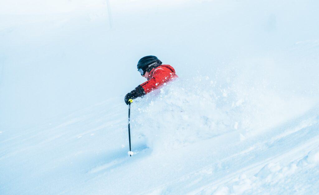 A skier wearing a red jacket skis through fresh powder