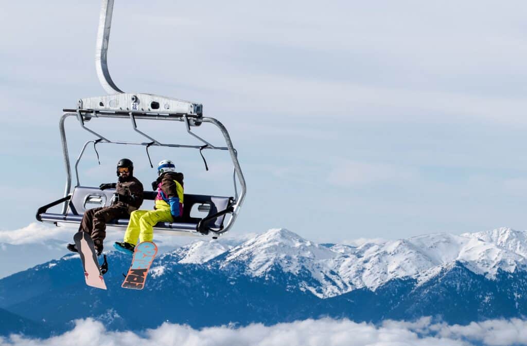 Two people sit on a
chairlift with mountains in the background