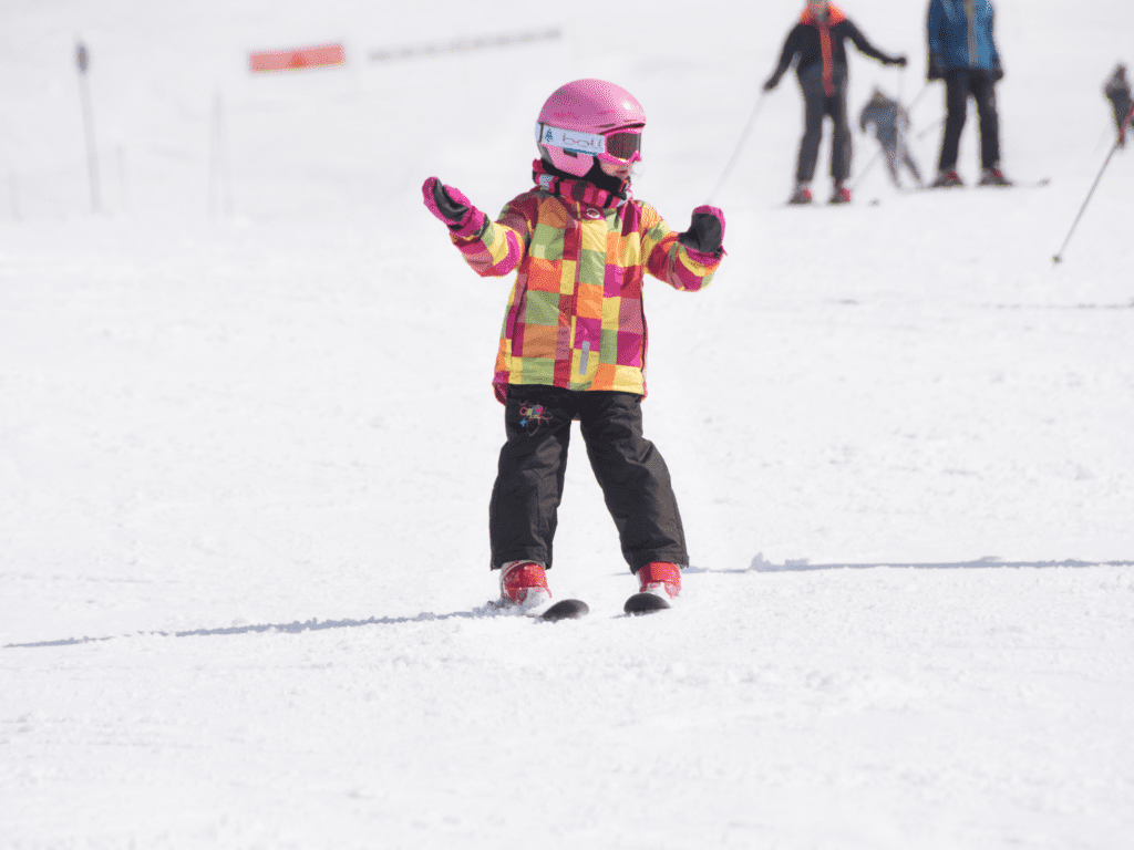 A young child skiing wearing a pink helmet and bright jacket.