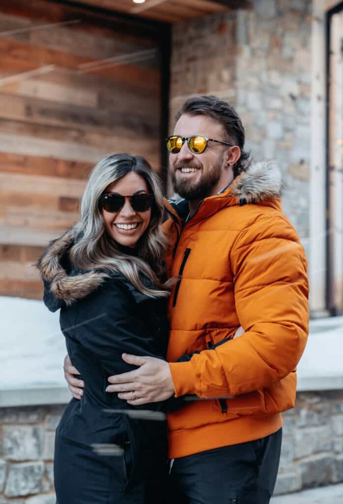 A happy couple stand outside a ski chalet