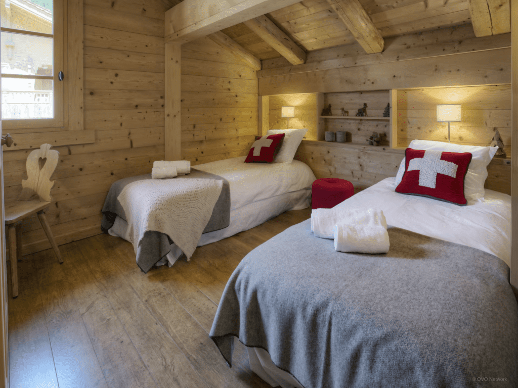 A twin room with shelved headboards above single beds with red cushions.