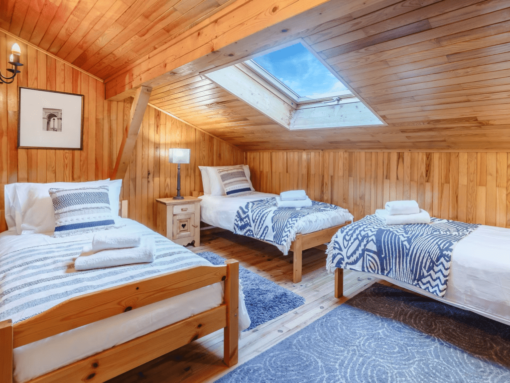 A triple bedroom with wooden walls and flooring and a skylight.