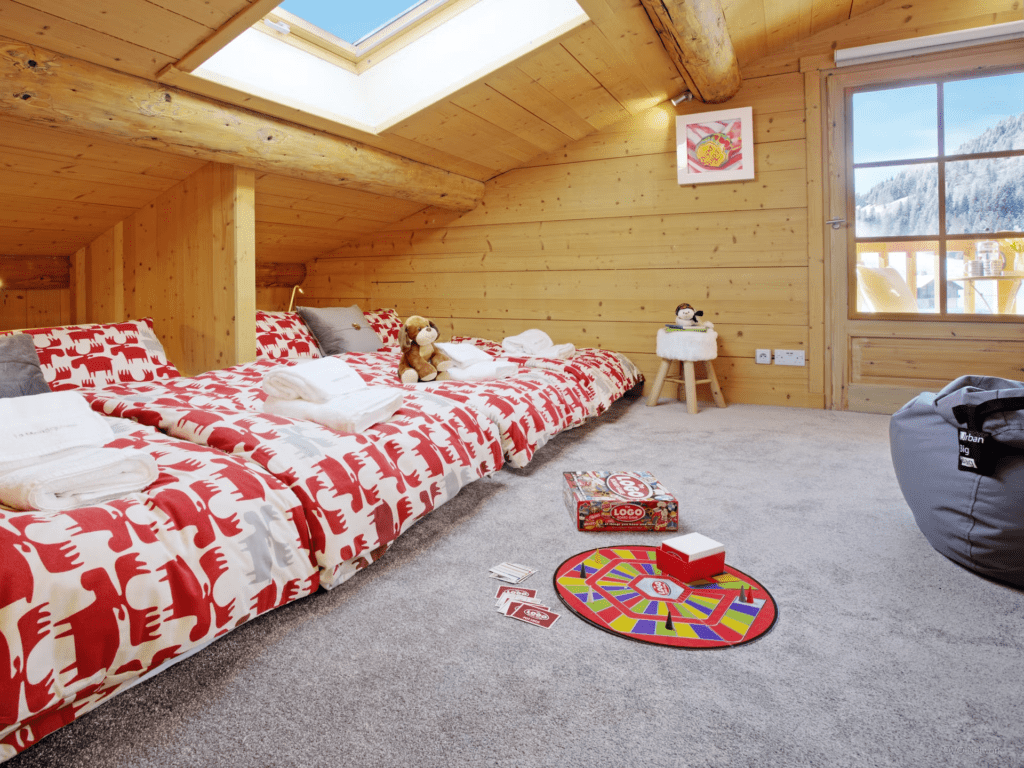 A kids dorm room with bright bed linen and a large window, with games on the floor.