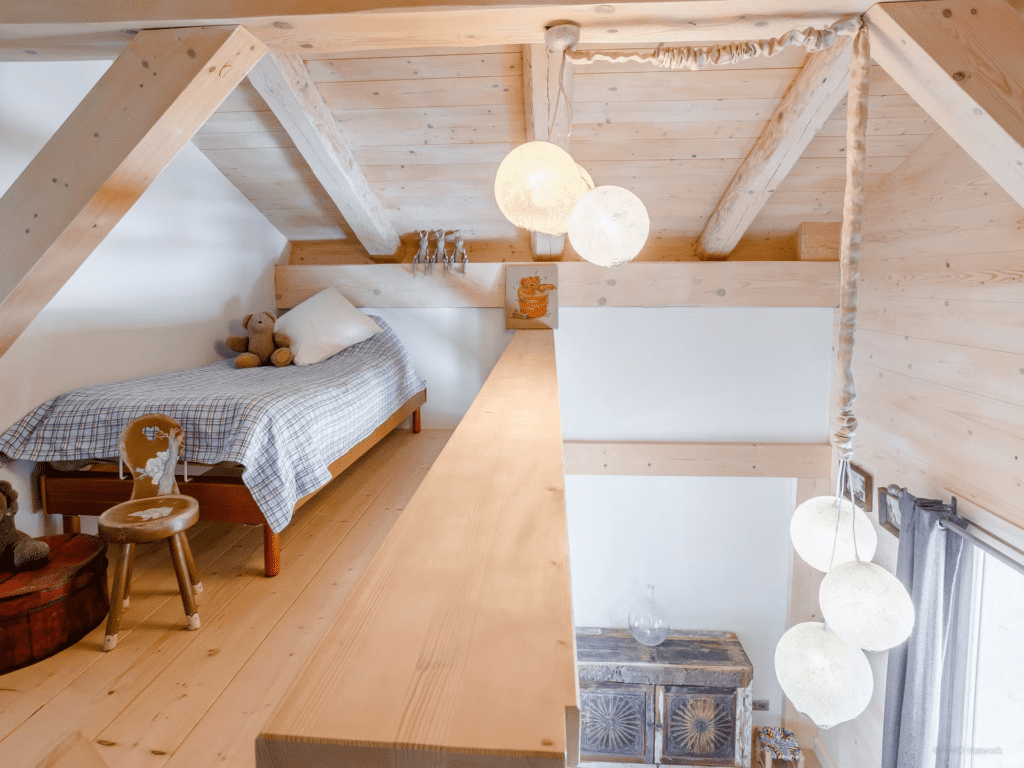 A sloped mezzanine bedroom for kids with a single bed and lantern lighting.
