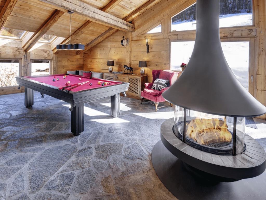 A sloped games room with a feature hanging fireplace, pool table and stone floor.