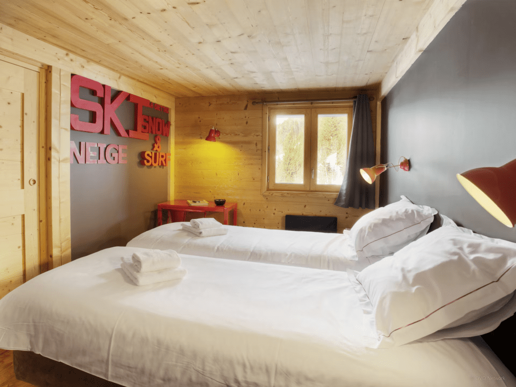 Red text art spelling 'ski', 'neige' and 'snow & surf' hang on a dark wall in a twin bedroom at Chalet Victorina
