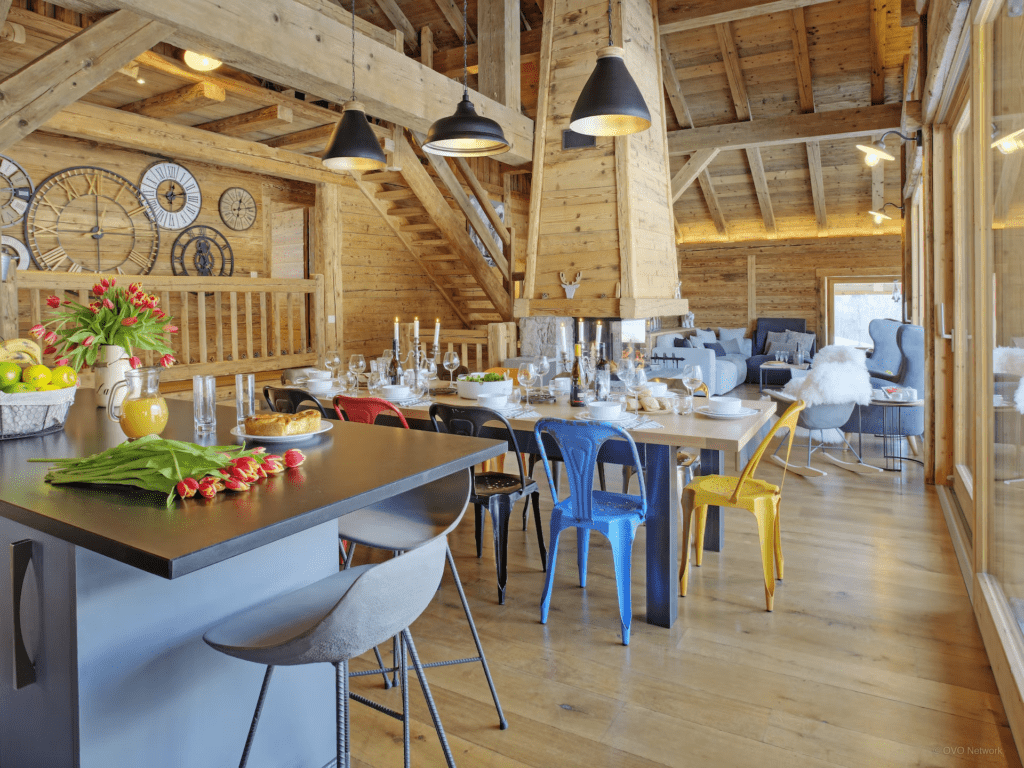 The dining space at a Ferme du Gran Shan with colourful chairs and a wall of clocks.