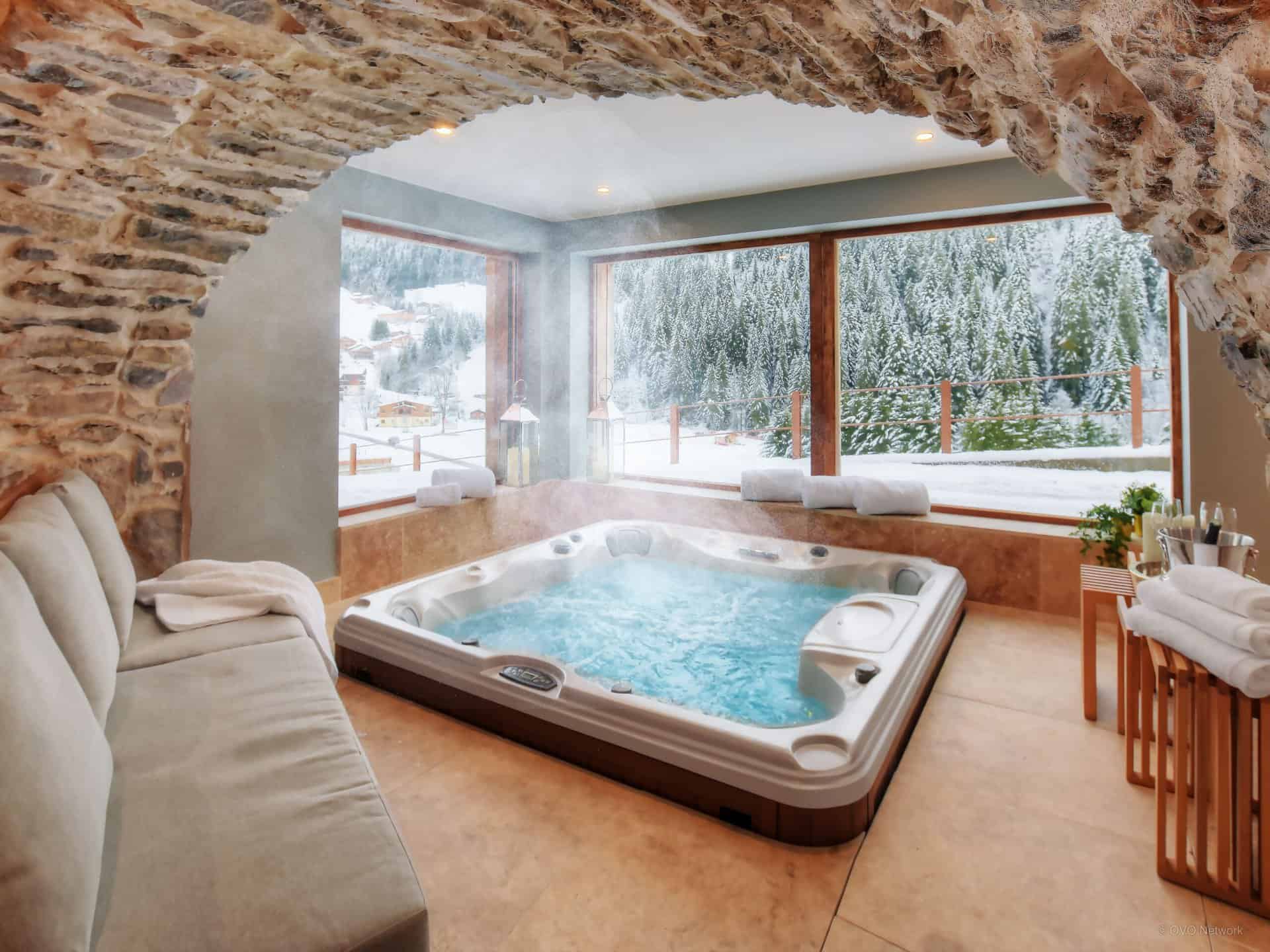 Charmante salle de jacuzzi dans un chalet dans les Alpes avec baies vitrées donnant sur le paysage. 