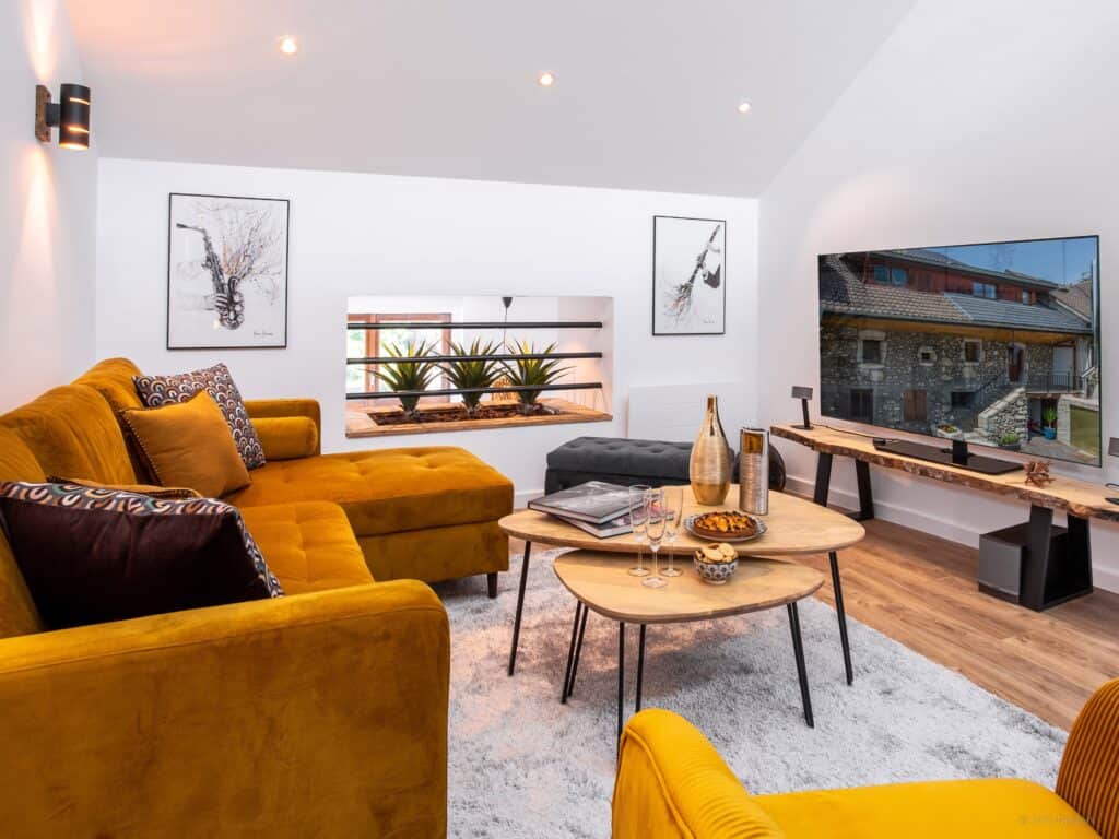 The living room at LoftYaute featuring a mustard coloured sofa, a pair of instrumental prints and a TV.