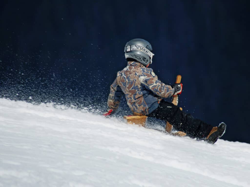 Un enfant en tenue de ski allant à toute vitesse sur une luge