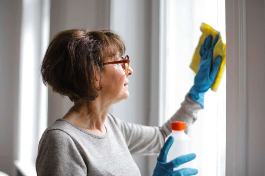 A woman holding cleaning products and polishing a window.