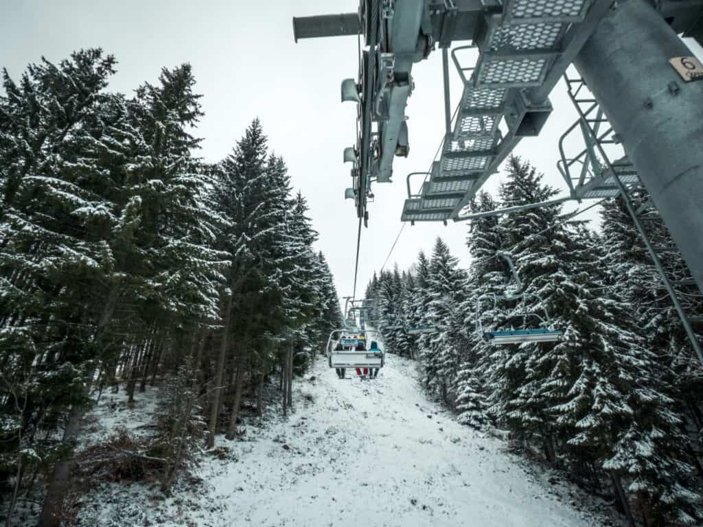 Skiers taking a chair lift through a snowy forest
