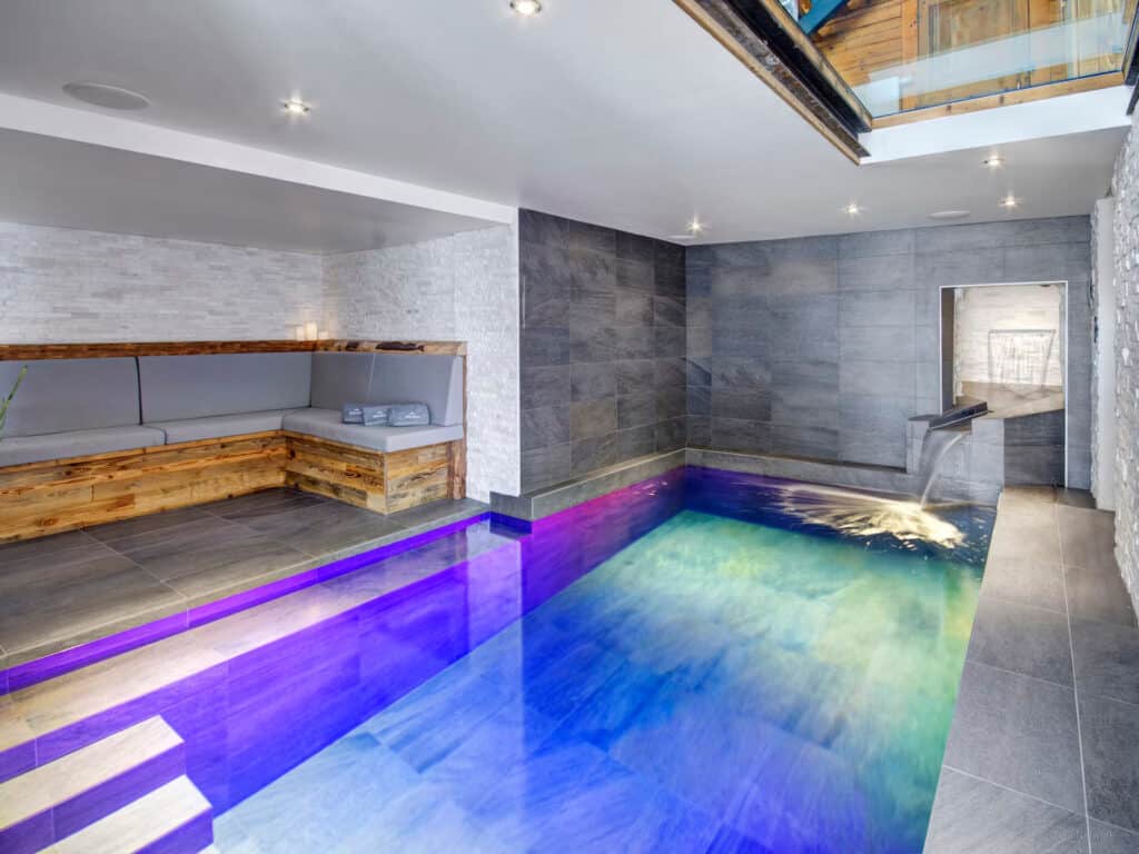 Photo d'une piscine intérieure d'un chalet, éclairée par des lumières bleues et violettes