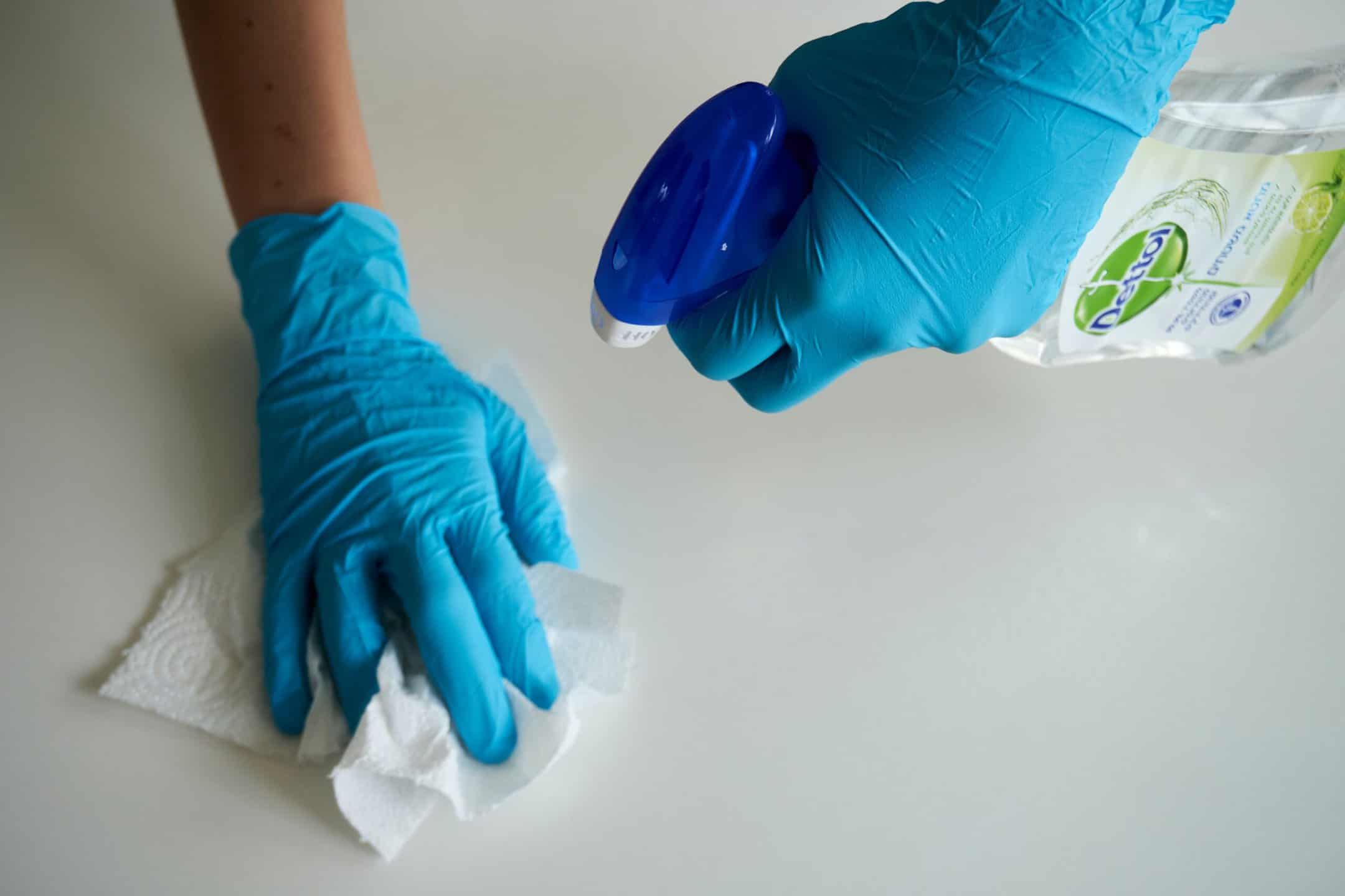 Mains gantées tenant une serviette et du produit de nettoyage.