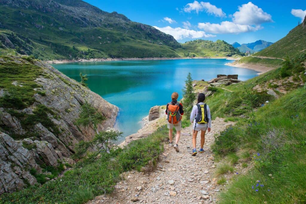 Two friends walk along a path near a blue Alpine lake