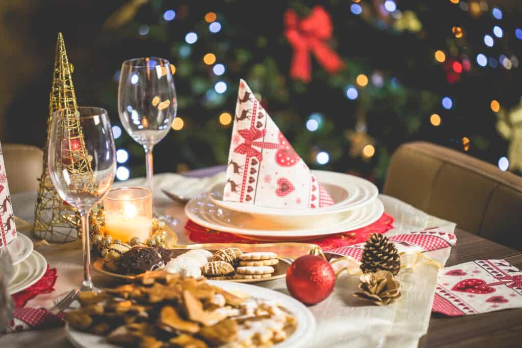 Une table joliment décorée pour Noël. On y trouve tous les éléments essentiels : pommes de pin, sablés, boules de Noël, bougies... dans les tons rouge et blanc.