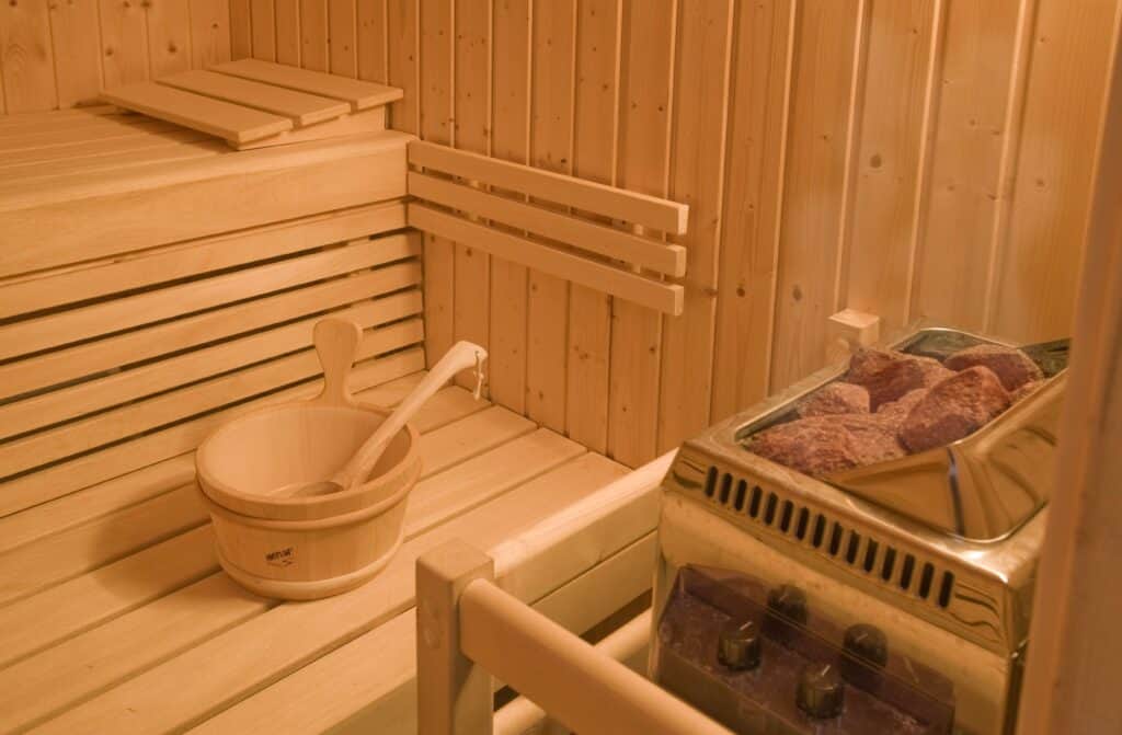 Intérieur en bois du sauna du Chalet Preta avec la bassine d'eau et les pierres chauffantes. 