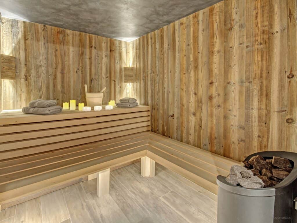 Un sauna construit en bois naturel avec un seau et une louche, des serviettes et des bougies.